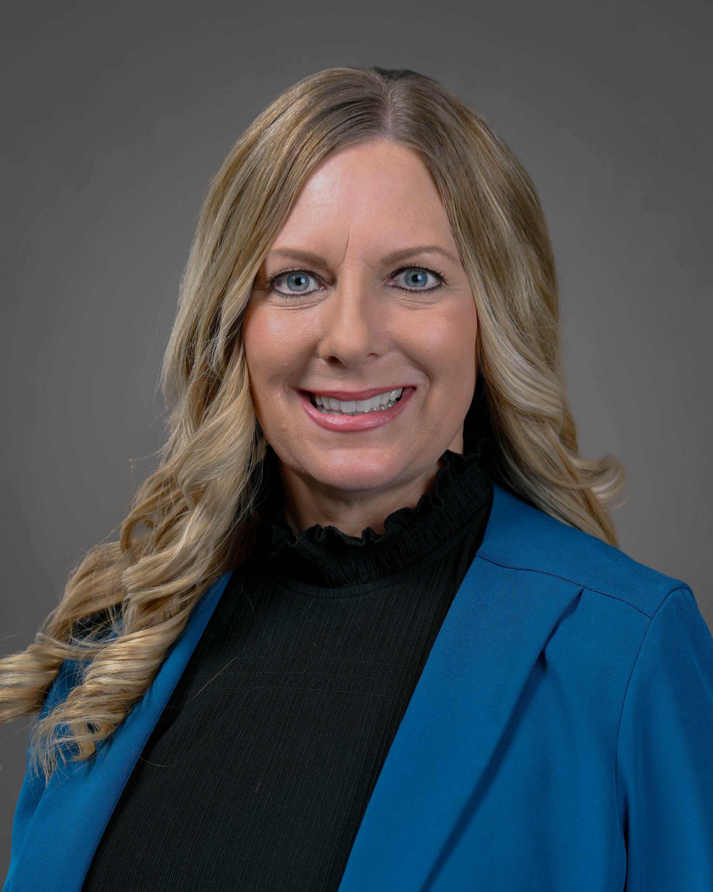 Blonde woman smiling wearing a black turtle neck and blue jacket.